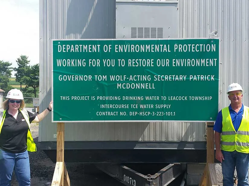 Project management team poses next to public signage